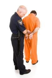 Man in jumpsuit being handcuffed by a policeman